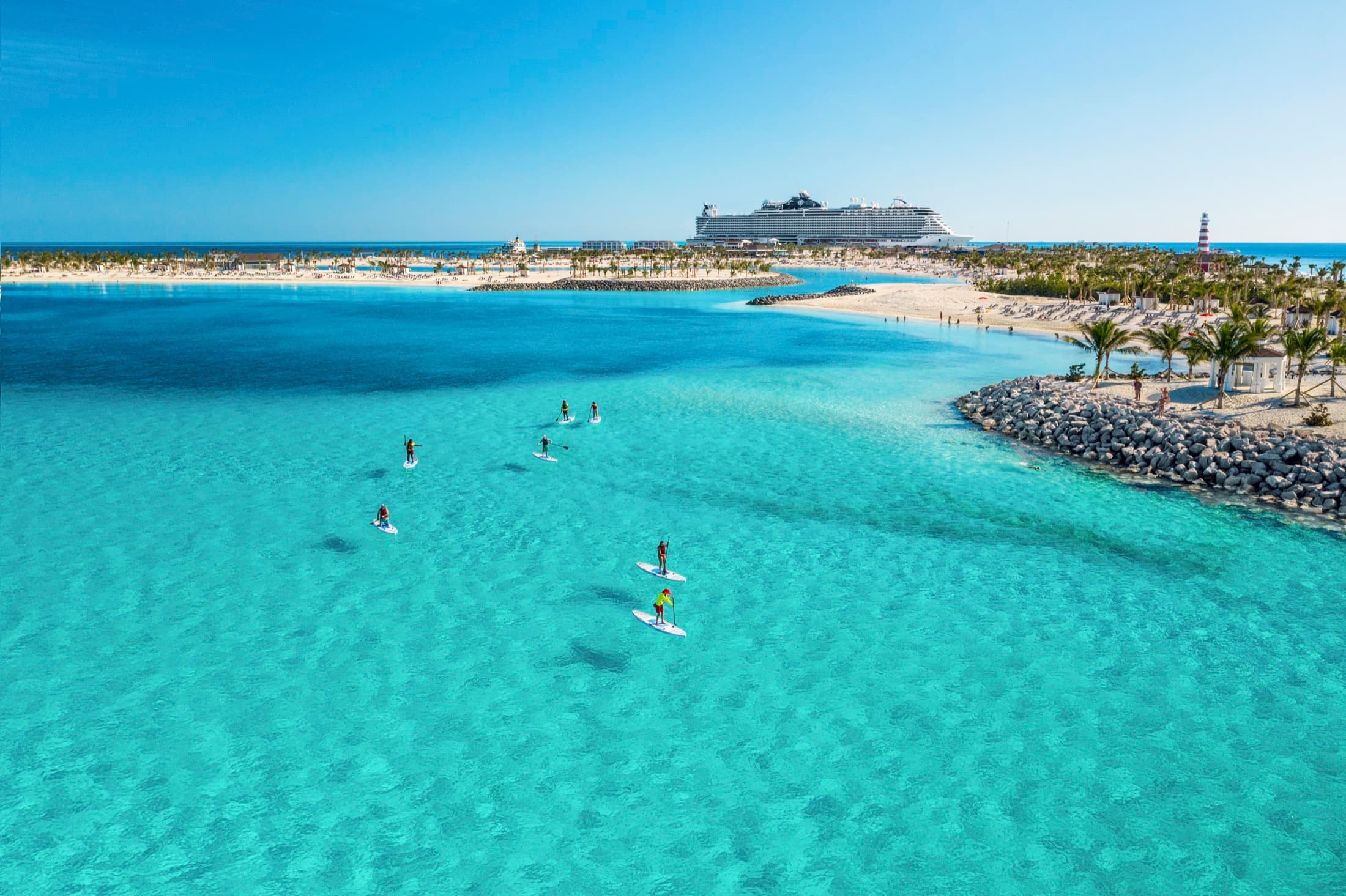 Paddleboarders in a turquoise lagoon at Ocean Cay in the Bahamas, with a cruise ship on the horizon